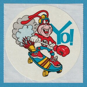 May include: A circular sticker featuring a cartoon character riding a skateboard. The character is wearing a red outfit, a helmet, and a boxing glove. The skateboard is blue and yellow, and the sticker has the word "Yo!" in blue.