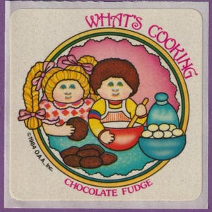 Może przedstawiać: Naklejka w stylu vintage z napisem "WHAT'S COOKING CHOCOLATE FUDGE". Przedstawia dwoje dzieci z kreskówek, jedno trzymające ciastko, drugie mieszające w czerwonej misce. Niebieska miska zawiera białe cukierki. Fioletowa obwódka.