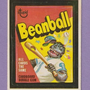 Peut inclure: Une carte de collection vintage de 1980 de Topps Chewing Gum, Inc. représentant un gorille de dessin animé portant un uniforme de baseball et tenant une batte. La carte est jaune et rouge avec le texte "Beanball" en grandes lettres jaunes. Le texte "All Cards The Same" et "Cardboard Bubble Gum" est également visible sur la carte.