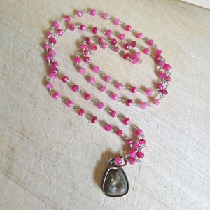 May include: A pink gemstone necklace with a silver chain and a pendant featuring a dark gray stone.
