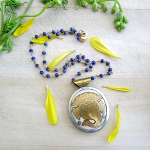 May include: A gold and white pendant necklace with a detailed elephant design. The necklace is made with blue lapis lazuli beads and a gold chain.