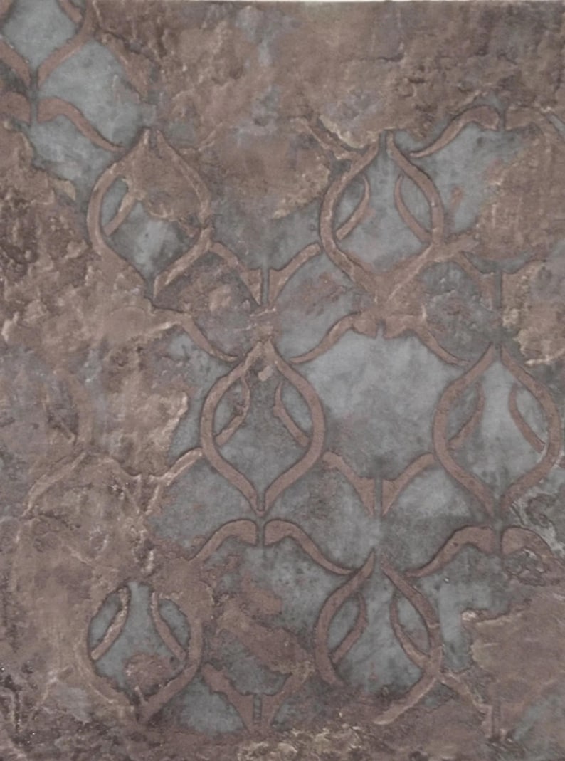 Puede incluir: Primer plano de una baldosa decorativa con un patr&oacute;n repetitivo. La baldosa tiene un aspecto moteado con tonos de gris, marr&oacute;n y un toque de azul. El patr&oacute;n es una serie de formas florales estilizadas interconectadas.