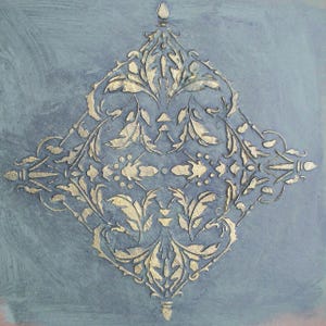 May include: A gold-colored, ornate floral design on a blue-grey background. The symmetrical pattern features leaves and other botanical elements within a diamond shape. The artwork has a textured appearance.