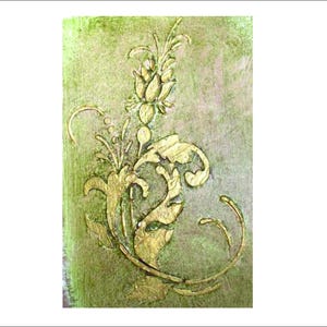 May include: Close-up of a decorative gold floral design on a textured, olive green background. The design features stylized leaves, a central flower, and curved accents, creating an elegant, vintage aesthetic.