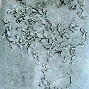 May include: A textured, gray-toned artwork featuring an embossed botanical design. The design showcases stylized leaves and vines, creating a natural, organic pattern. The artwork has a rustic, aged appearance.