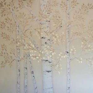 May include: A wall art piece featuring a stylized depiction of birch trees. The trees have white bark with black markings and are adorned with gold-colored leaves. The background is a soft, neutral tone.