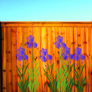 May include: A wooden fence with vertical planks is painted with purple iris flowers and green stems. The fence is stained a warm brown color, and the sky is a clear blue.