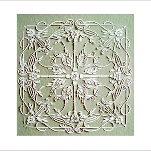 May include: A square, white paper cut-out with an intricate floral and leaf design. The artwork features symmetrical patterns of flowers, vines, and decorative flourishes on a pale green background. The design is detailed and delicate.