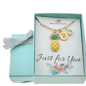May include: A light blue gift box with a white card inside. The card has a gold pineapple charm necklace with a green and yellow pineapple charm, a gold initial charm, and a green gemstone charm. The card says "Just for You".