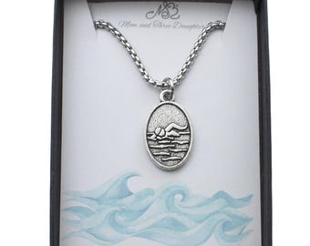 May include: Silver-toned necklace with an oval pendant featuring a mountain and water scene. The necklace is displayed in a black gift box with a card that has a wave design and the text "Mom and Three Daughters" and "www.momandthree.com".