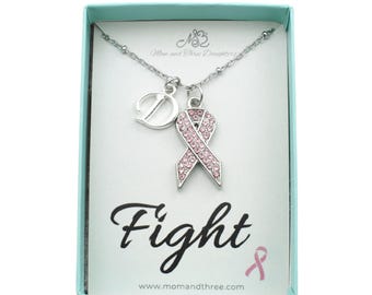May include: A silver necklace with a pink ribbon pendant, a letter "D" charm, and the word "Fight" on the card. The ribbon is encrusted with small pink crystals. The card is in a light blue box.