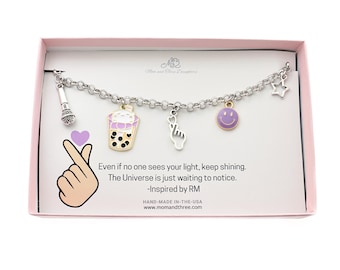 May include: A silver charm bracelet with various charms, including a microphone, a boba tea cup, a hand gesture, a smiley face, and a star. The bracelet is displayed in a pink box with text that reads "Even if no one sees your light, keep shining."