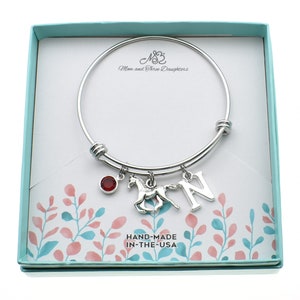 May include: A silver bangle bracelet with a red gemstone, a horse charm, and a letter "N" charm. The bracelet is in a light blue box with the text "Mom and Three Daughters" and "HAND-MADE IN-THE-USA".