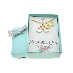 May include: A turquoise gift box with a white ribbon and a card that says "Just for You". Inside the box is a gold necklace with a rainbow charm, a letter charm, and a green gemstone charm.