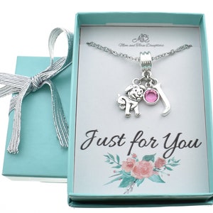 May include: A silver necklace with a charm of a dog, a pink crystal, and the letter J. The necklace is in a light blue gift box with a white background and the words "Just for You" printed on it.