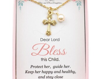 May include: A gold-colored cross pendant necklace with a pearl charm, displayed on a pink card. The card has the text "Dear Lord Bless this Child." and a prayer. The necklace is in a pink box.