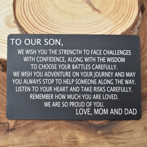 May include: A black metal card with white text that reads "To our son, We wish you the strength to face challenges with confidence, along with the wisdom to choose your battles carefully. We wish you adventure on your journey and may you always stop to help someone along the way. Listen to your heart and take risks carefully. Remember how much you are loved. We are so proud of you. Love, Mom and Dad."