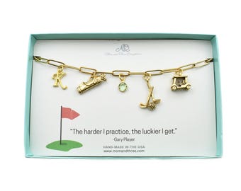 May include: Gold-toned charm bracelet with golf-themed charms, including a golf bag, golf cart, and golf clubs. The bracelet is displayed in a teal box with the quote "The harder I practice, the luckier I get."