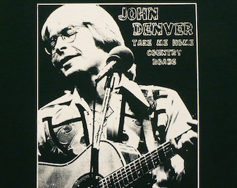 May include: Black and white image of John Denver holding a guitar and singing into a microphone. The text "JOHN DENVER TAKE ME HOME COUNTRY ROADS" is printed on the image.
