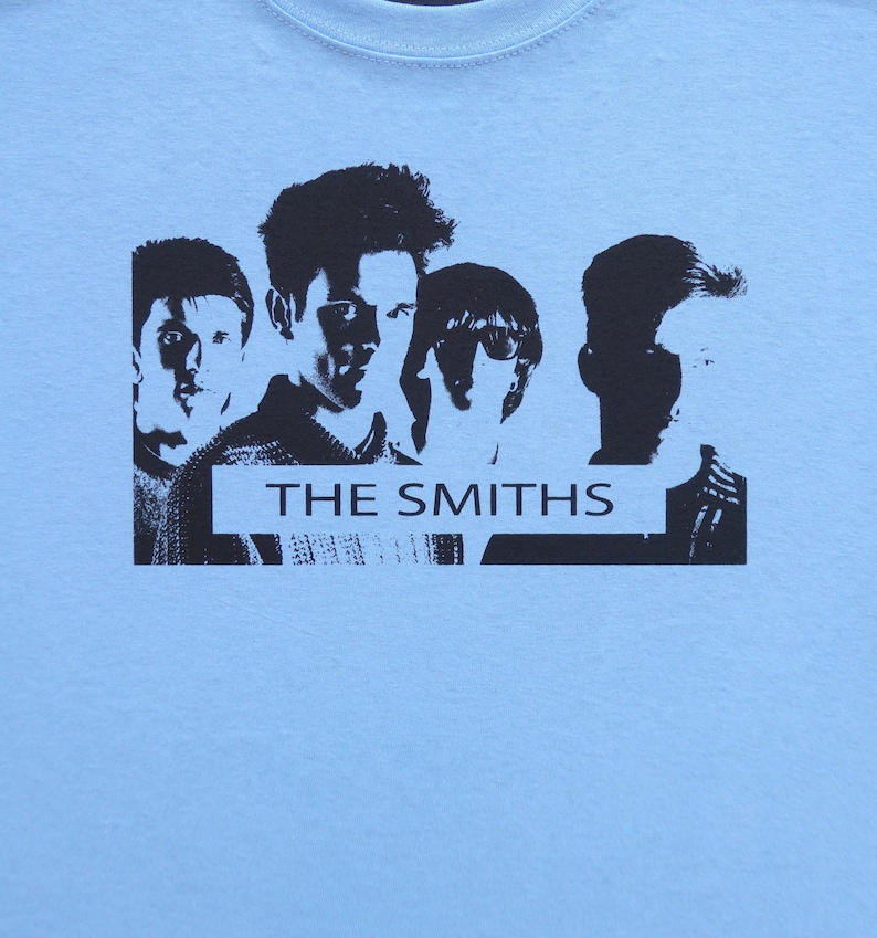 May include: A light blue t-shirt with a black and white silhouette image of the band The Smiths. The band members are arranged in a row with the band's name in a black banner below them.