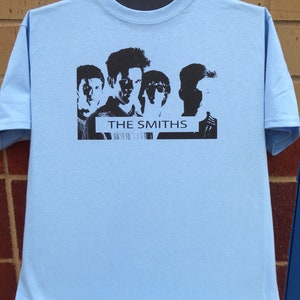 May include: Light blue t-shirt with a black and white image of the band The Smiths. The image features five band members in silhouette.