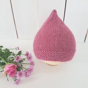 May include: A pink knitted baby hat with a pointed top. The hat is made of a soft, fuzzy yarn and has a simple, classic design.