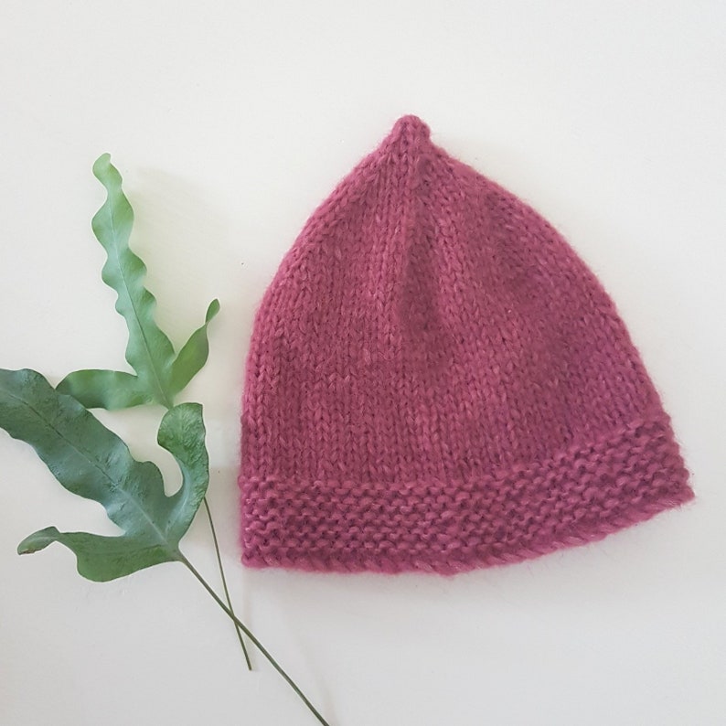 May include: A knitted hat in a deep pink colour. The hat has a simple design with a pointed crown and a folded brim.