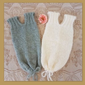 May include: Two knitted baby sleeping sacks, one in a light green color and the other in a cream color. Both sacks have a tie at the bottom.