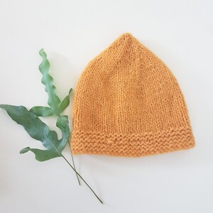 May include: A knitted beanie hat in a mustard yellow colour. The hat has a simple design with a ribbed brim.