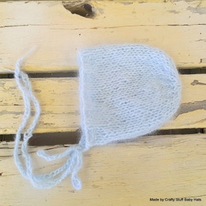 May include: A light blue baby bonnet with a fuzzy texture and a long tie. The bonnet is made of soft yarn and is perfect for a newborn baby.