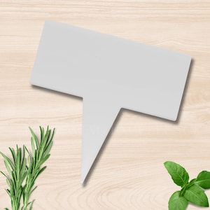 May include: A white plastic plant marker with a rectangular top and a pointed bottom. The marker is designed to be inserted into the soil to identify herbs and plants. Rosemary and basil are visible in the background.