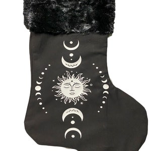 May include: Black Christmas stocking with a white sun and moon design. The stocking has a black faux fur cuff.