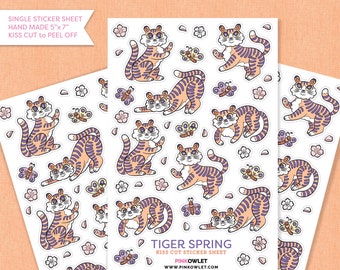 Puede incluir: Una hoja de pegatinas recortadas con un patrón repetido de tigres de dibujos animados naranja y morado con detalles de mariposas y flores. La hoja está etiquetada como "Tiger Spring Kiss Cut Sticker Sheet" con el sitio web "www.pinkowlet.com".