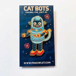 Puede incluir: Pin esmaltado con un diseño de gato robot. El pin es principalmente azul, naranja y dorado, con el texto "CAT BOTS" y "ENAMEL PIN_UNIT 03" en la parte superior. Está sobre una tarjeta azul oscuro con un fondo estrellado y el sitio web www.pinkowlet.com.