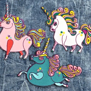 Op de afbeelding: Drie geborduurde strijkpatches met kleurrijke eenhoorns met draaiende manen en staarten. De eenhoorns zijn roze, wit en turquoise.