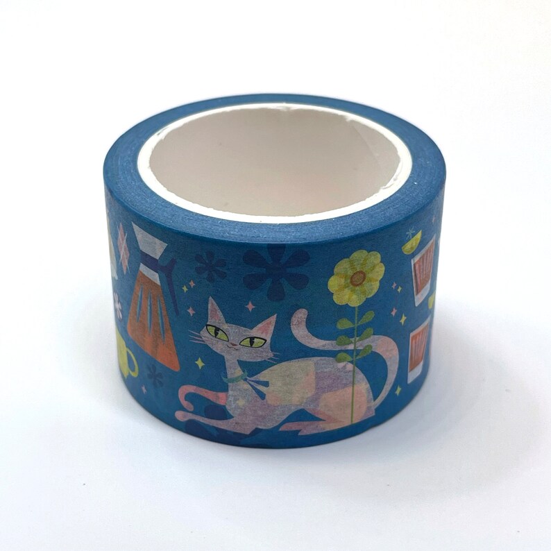 May include: A blue washi tape roll with a design featuring a cat, flowers, and a coffee pot. The cat is light pink and white with blue eyes. The flowers are yellow and orange. The coffee pot is brown and orange.