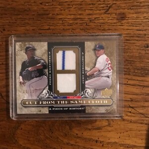 Könnte beinhalten: Baseball-Sammelkarte mit Pedro Martinez und Curt Schilling. Die Karte hat einen goldenen Hintergrund mit Bildern der Spieler und einem Stoffstück. Der Text auf der Karte lautet "CUT FROM THE SAME CLOTH" und "A PIECE OF HISTORY."