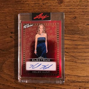 May include: A red Leaf Fame Electrum trading card featuring Helen Hunt in a strapless blue dress. The card has a gold star border and a signature. The card is encased in a clear protective holder.