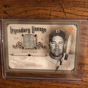 May include: A baseball card featuring Duke Snider, a baseball player for the Brooklyn Dodgers. The card is gold and brown with the text "Legendary Lineage" and "Duke Snider".