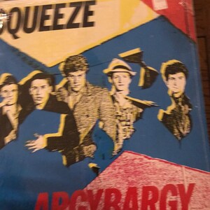 May include: Album cover for the band Squeeze, titled "Argybargy." The cover features a blue background with geometric shapes in yellow and red. The band members are depicted in a stylized illustration.