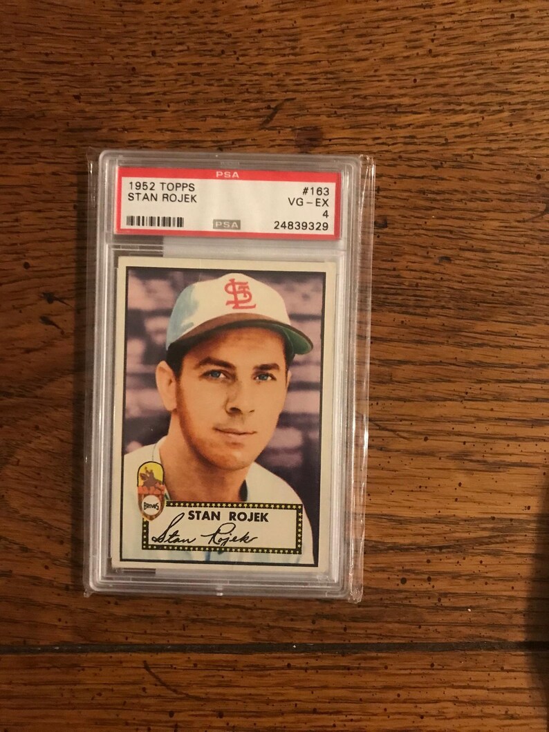 May include: A 1952 Topps Stan Rojek baseball card, graded VG-EX 4 by PSA, encased in a protective holder. The card features a portrait of Stan Rojek wearing a baseball cap with a red logo. The card is set against a light background.