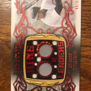 Può includere: Una carta da baseball rossa e dorata con l'immagine di un giocatore di baseball che indossa una divisa bianca e nera. La carta presenta un anello dorato con le parole "Ring Leaders" e "4" su di esso. La carta è numerata 48/50. Il nome del giocatore è Bernie Williams.