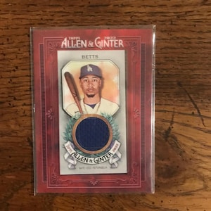 May include: A red baseball card with a white border featuring a baseball player wearing a blue jersey with a white 'LA' logo. The card is titled "Topps Allen & Ginter 2022" and features the player's name "Betts".