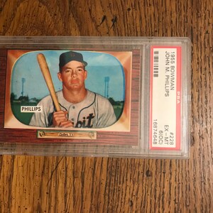 Puede incluir: Una tarjeta de béisbol Bowman de 1955 con John M. Phillips, un jugador de béisbol que sostiene un bate. La tarjeta está calificada como EX-MT por PSA y tiene el número 16874648.