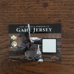 Könnte beinhalten: Baseballkarte mit Barry Bonds von den San Francisco Giants. Die Karte trägt die Aufschrift "100% Authentic Memorabilia" und "Game Jersey". Die Karte hat ein kleines Stoffquadrat von einem Spieltrikot.