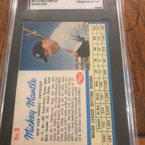 May include: A 1962 Post Cereal Mickey Mantle baseball card, number 5, encased in a black SGC slab. The card features a photograph of the player, biographical text, and a major league batting record table. The label at the top reads Authentic.