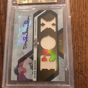 May include: A 2008 Topps Triple Threads Duke Snider baseball card in a Beckett graded plastic case. The card features a blue ink autograph, a photograph of the player, and three fabric relic cutouts. The label indicates a 9.5 Gem Mint grade.