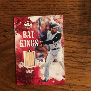 May include: A baseball card with the text "BAT KINGS" in red and white. The card features an illustration of a baseball player in a white uniform with the number 11. The player is holding a bat. The card also has the name "BARRY LARKIN".