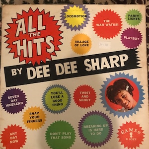 May include: A vintage vinyl record album cover featuring Dee Dee Sharp. The cover is white with a red starburst design and the text "All the Hits by Dee Dee Sharp". The album cover features a variety of song titles in colorful starburst designs, including "Locomotion", "Village of Love", "The Wah Watusi", "Party Lights", "Playboy", "Seven Day Weekend", "Any Day Now", "Snap Your Fingers", "You'll Lose a Good Thing", "Twist and Shout", "Don't Play That Song", "Breaking Up is Hard to Do", and "Gameo".