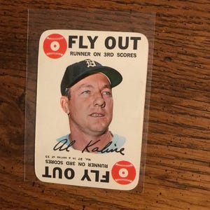 May include: Vintage baseball card featuring Al Kaline, with the text "FLY OUT" and "RUNNER ON 3RD SCORES." The card has a portrait of Kaline wearing a baseball cap. The card is in a protective sleeve.